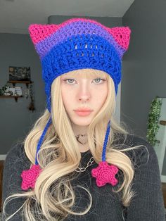 a woman with long blonde hair wearing a blue and pink knitted cat ear flap hat