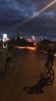 two bicyclists riding down the street at night