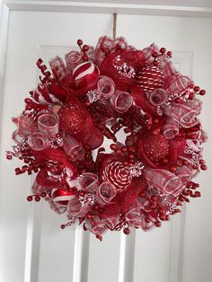 a wreath hanging on the front door decorated with candy canes and red glass ornaments