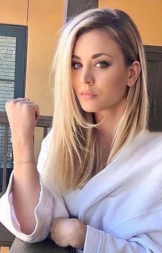 a woman with long blonde hair sitting in a chair and looking at the camera while wearing a white robe