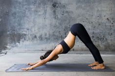 a woman is doing a yoga pose on a mat in front of a concrete wall