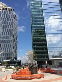 an orange bench in the middle of a circular area near two tall buildings with glass windows