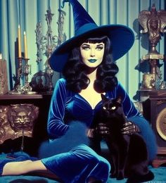 a woman sitting on the floor next to a black cat wearing a witches hat and blue dress