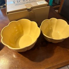 two yellow bowls sitting on top of a wooden table next to an open cardboard box