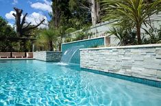 an outdoor swimming pool surrounded by trees and water features a waterfall that runs down the side of it