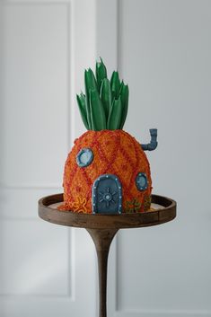 there is a cake that looks like a house on top of a wooden stand in the shape of a pineapple