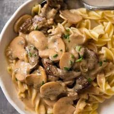 a bowl filled with pasta and mushrooms covered in gravy on top of a table