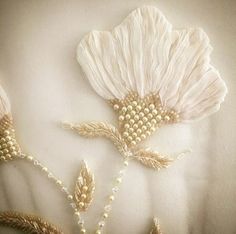 two white flowers with pearls and beads on the petals are in front of a beige background