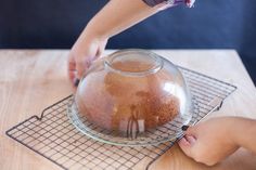 a person is placing something in a bowl on a wire rack with another hand reaching for it