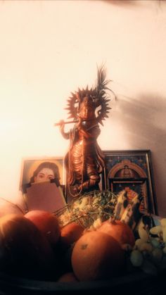 a bowl filled with fruit next to a statue on top of a table in front of a wall