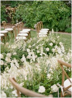 rows of chairs are lined up in the middle of a field with white flowers and greenery