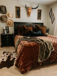 a bed with brown and black comforter in a bedroom next to a cow skull on the wall