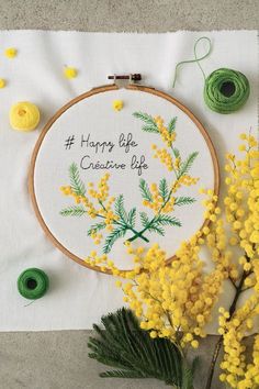 yellow flowers and green thread on a white table cloth with embroidered saying happy life creative life