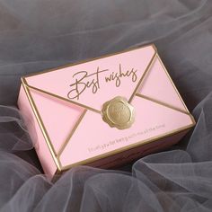 a pink and gold box with the word best wishes written on it sitting on a tulle