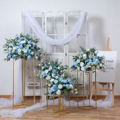 three blue and white flowers in vases next to an easel on a wooden floor