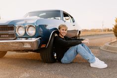 a man sitting on the ground next to a car with his arms crossed and smiling