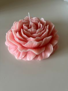 a pink flower sitting on top of a white table next to a candle with a stick sticking out of it