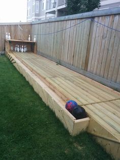 a wooden bench sitting on top of a lush green field next to a fence with bowling balls in it