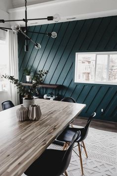 a wooden table with black chairs in front of a green paneled wall and window