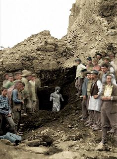 a group of people standing on top of a dirt hill next to a small cave