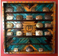 Trophy buckle display case. Quilt wood pattern style. Custom patterns and colors. The 30x30 will hold about 29 buckles depending on size of the buckles and if you put them across the bottom of the frame as well as the middle shelves. Lipped shelves for buckles to display upright. Can add custom painted logo/brand or initials to center. All over clear gloss. Floral nickle studs, antique brass daisies or antique hammered brown stud borders. 30x30 $340 All images are stock photos of past cases. The Belt Bucket Display, Belt Buckle Shadow Box Display Case, Buckle Shelf Display, Buckle Case Display, Buckle Box Display Case, Belt Buckle Display Case