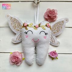 a tooth fairy ornament hanging on a white wooden wall with flowers around it