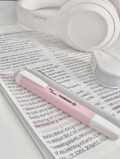 a pink pen sitting on top of a piece of paper with headphones next to it