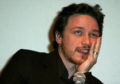 a man holding his hand to his face while sitting in front of a white wall