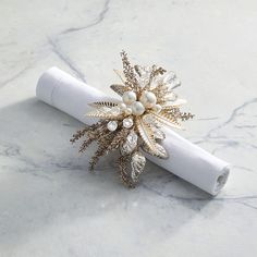 a white napkin with a gold flower and pearls on it sitting on a marble surface