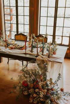 a table with flowers and candles on it in front of two large windowed windows