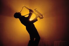 a man playing an instrument in front of a yellow background with the sun behind him