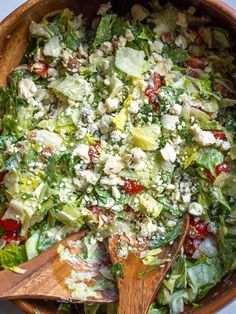 a salad with lettuce, tomatoes and feta cheese in a wooden bowl