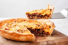 a person cutting into a meat and cheese quiche on top of a wooden cutting board