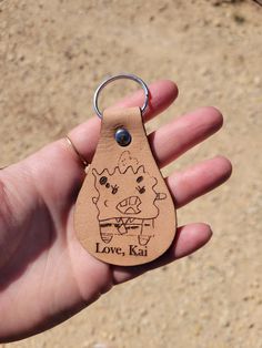 a hand holding a leather keychain with a drawing on it