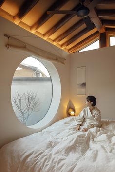 a person sitting on a bed in front of a round window