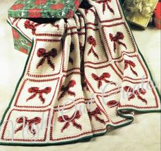 a crocheted christmas blanket with bows on it and a gift box in the background