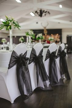 the chairs are lined up with black sashes on them for an elegant wedding reception