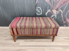 a striped bench sitting on top of a hard wood floor next to a flowered wall