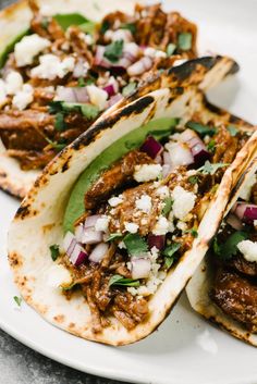 three tacos with meat, onions and feta cheese on them sitting on a white plate