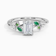 an emerald and diamond engagement ring with leaves on the band, set in white gold