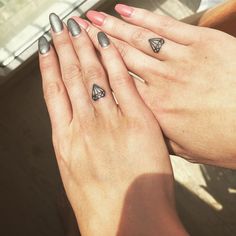 two hands holding each other with tattoos on their fingers and one has a diamond ring