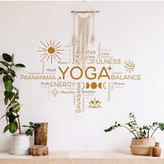 there is a wall decal that says yoga in many languages on the wall next to some potted plants