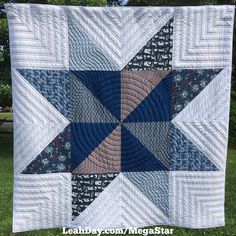 a blue and white quilt hanging on the side of a tree in front of some grass