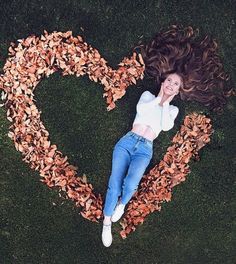 a woman laying on the ground with her hair in the shape of a heart surrounded by leaves