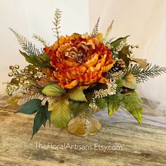 an arrangement of flowers and greenery on a wooden table