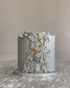 a white and gold cake with flowers on it sitting on a marble countertop next to a gray wall