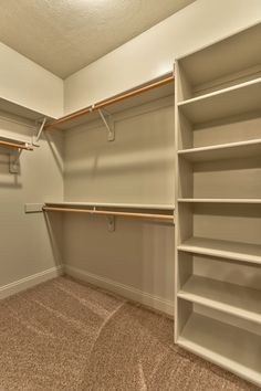 an empty walk in closet with white shelving and tan carpeting on the floor