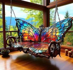 a stained glass butterfly sitting on a swing in front of a window with chains hanging from it's sides