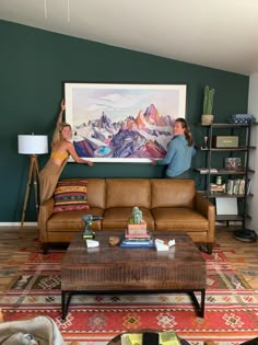 two people standing in front of a painting on the wall next to a couch and coffee table