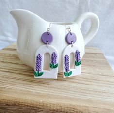 a pair of purple and white earrings sitting on top of a wooden table next to a vase